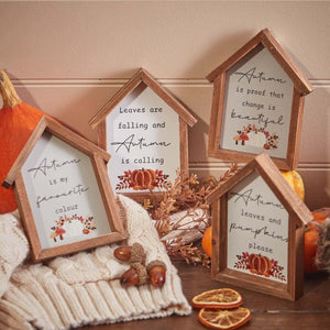 Cozy rustic autumn decor featuring the Autumn Pumpkin House Framed Sign With Quotes, surrounded by pumpkins, dried orange slices, and fall leaves. A beige knitted blanket adds warmth to the scene. Quotes highlight the beauty of autumn and the appeal of leaves and pumpkins.