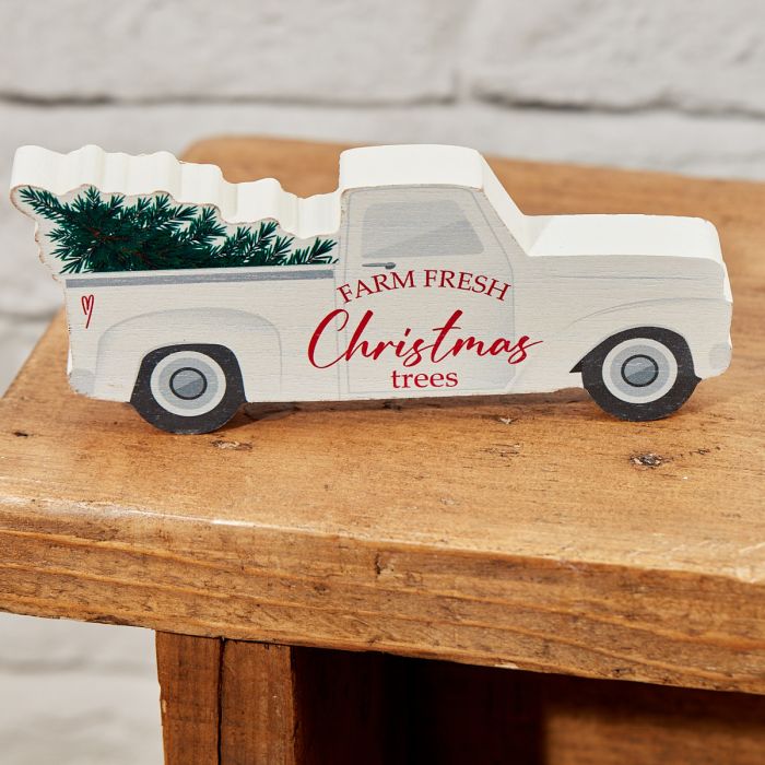 The Christmas Wooden Lorry with Festive Tree is a charming wooden decorative piece shaped like a vintage truck, painted white with red text that reads "FARM FRESH Christmas trees," and carrying a festive tree in the back. This delightful decoration sits on a wooden surface against a lightly textured background, making it perfect for festive decor.