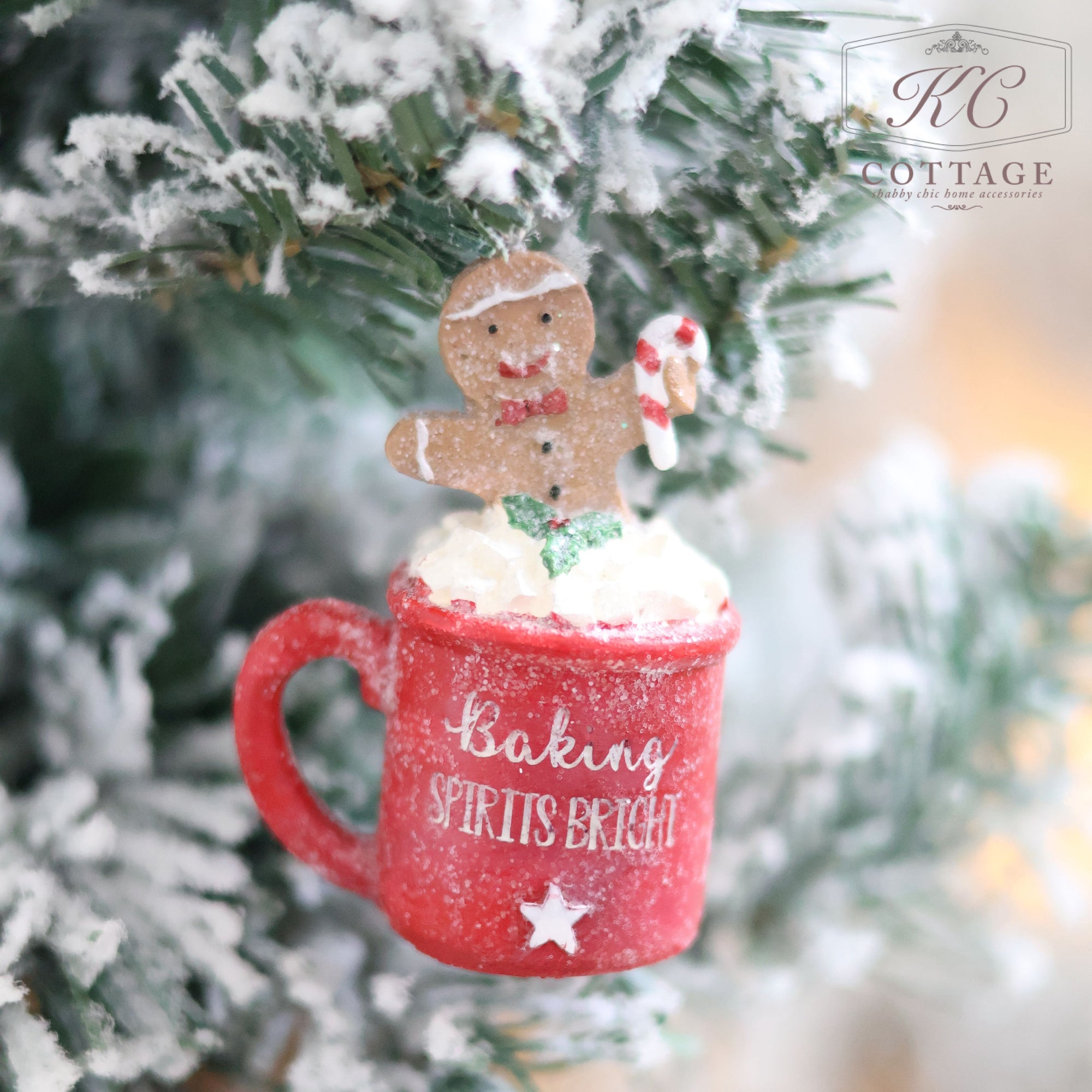 A Christmas Gingerbread & Mug Hanging Tree Ornament featuring a red gingerbread mug adorned with "Baking Spirits Bright" sits on a snowy branch. It holds a gingerbread figure with a candy cane and is accompanied by a cheerful marshmallow snowman.