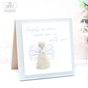 A square card with a light gray background and the text "Angels up above watch over us with love." It features a simplistic angel made of stone-like material, outlined with purple wings. Perfect for home decor, the Pebble Angel Forever Cards logo is in the top left corner.