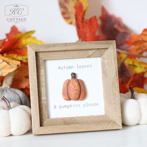 The Autumn Pumpkin 3D Framed Plaque With Quotes, adorned with a small pumpkin decoration and reading "Autumn leaves & pumpkins please," stands among white mini pumpkins and colorful autumn leaves. The background features a wall with a "KC Cottage" logo, creating the perfect Pumpkin Decor display for your home.