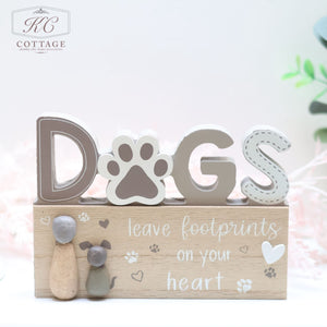 The "Dog Pebble Signs" are a charming addition to any dog lover's home. Featuring the word "DOGS" with a paw print representing the "O," this decorative sign includes a wooden plaque at the bottom that reads, "Leave footprints on your heart," embellished with small paw prints and two dog figurines. The KC Cottage logo is delicately placed at the top left corner.