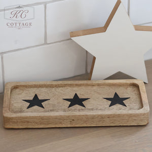 The kitchen exudes rustic charm with a Rectangle Rustic Wooden Tray from the Hearts & Stars collection, featuring three black stars, placed on the countertop. In the backdrop, a white wooden star complements the scene against the white tiled walls.