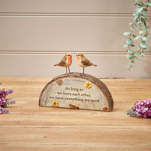 An Autumn Robin Couple On Resin Bark Base features two small, colorful birds atop a resin bark base. Below them, an engraved message reads, "As long as we have each other, we have everything we need." The piece is surrounded by purple and green floral accents on a light wood surface, perfect for nature lovers.