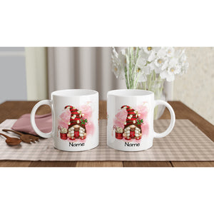 Two *Personalised Christmas Gonk Mugs* with a whimsical gnome house design and customizable "Name" text at the bottom are placed on a light-checked tablecloth. Each mug features vibrant colors and intricate details. Beside the mugs, some wooden utensils and a vase with white flowers in the background add a festive touch.
